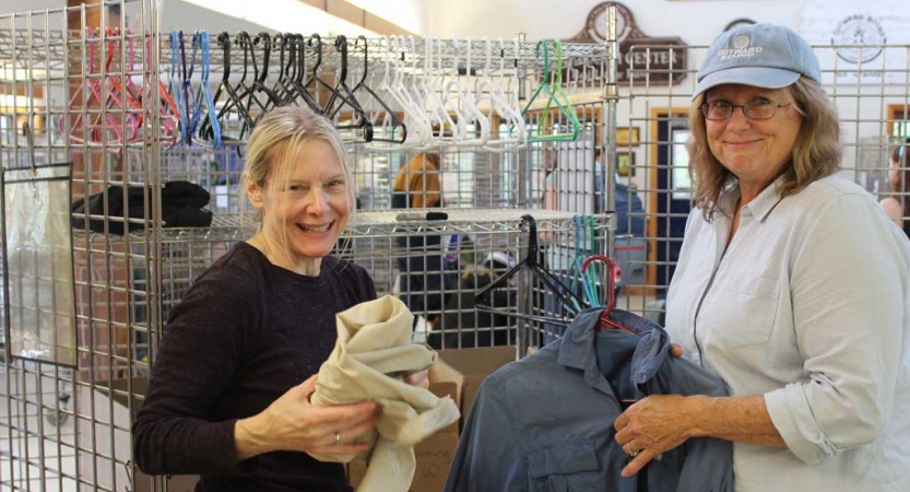 Two people smile at the camera while organizing clothing during a service project with Outward Bound. 